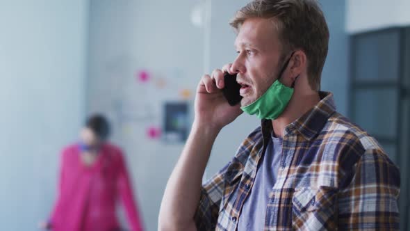 Caucasian man with face mask talking on smartphone in office