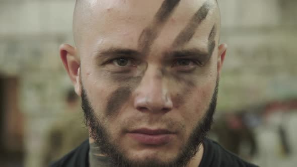 Close Portrait of Strong Fighter with Soot Strips on Face Looks at Camera