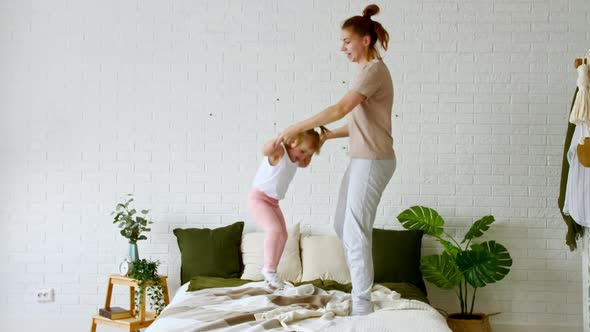 Young Mom and Child Little Daughter Jumping on the Bed