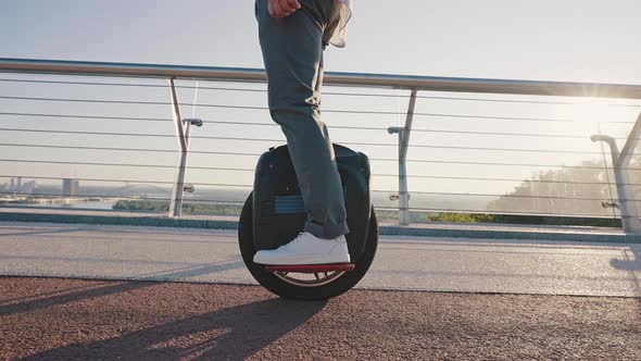 Man Rides Electric Unicycle on Footbridge Against City View