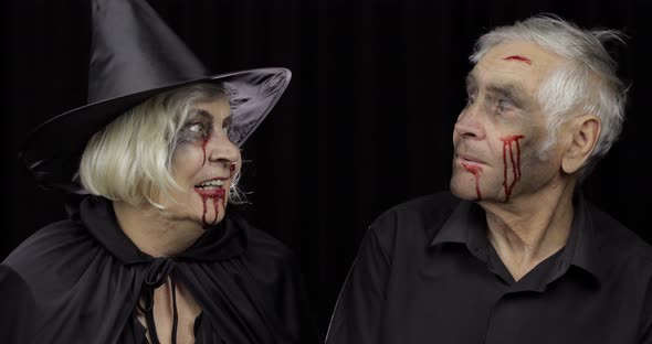 Elderly Man and Woman in Halloween Costumes Making a Kiss. Witch and Zombie