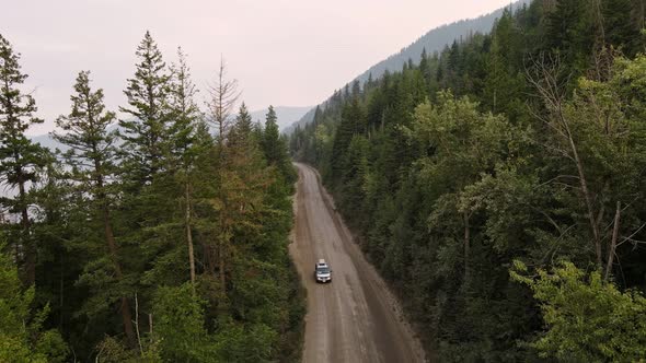 Drone footage of a car driving through a dry boreal forest in British Columbia at sunset. Aerial opp