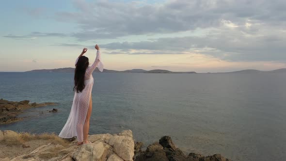 Young woman approaches edge of rocks admiring sunrise on sea