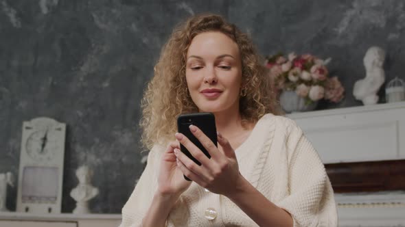 Young Adult Caucasian Woman Thinking and Typing on Her Smart Phone Indoors