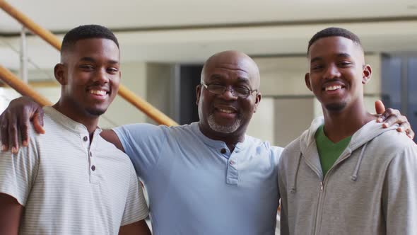 Portrait of african american senior father and twin teenage sons embracing and smiling
