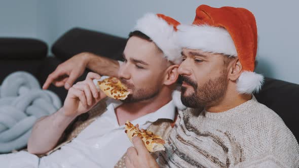 Lovely Gay Male Couple with Christmas Hats Eating Pizza and Watching Movies on the Christmas Eve