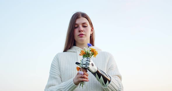 Teenager with a Disability Holds a Bouquet of Wild Flowers with Her Bionic Hand Against the Sky and