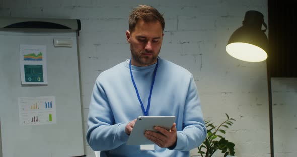 A Man Smiles Looking at the Camera Interrupted From Work at Tablet in Office