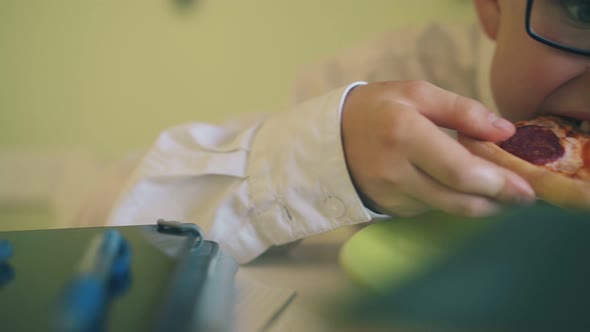 Cute Boy in Glasses Has Lunch with Pizza at Table Closeup