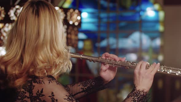 Blonde Woman Playing Flute on a Background of Stained Glass Windows