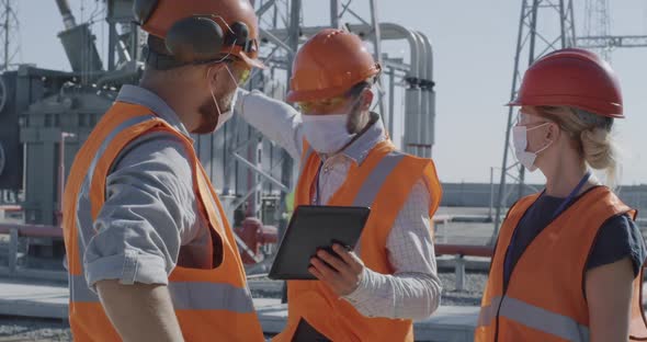 Male Workers in Masks Using Tablet Together on Power Station