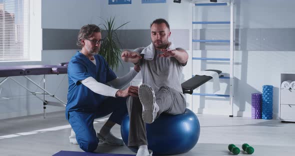 Middle Aged Therapist Helping Patient to Balance on Fit Ball