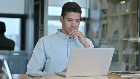 Young African Man Thinking and Working on Laptop