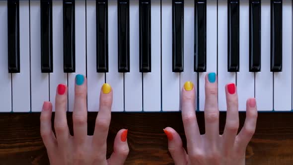 A Young Positive Girl with Beautiful Hands and a Color Manicure Plays Piano