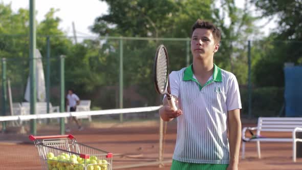 A Young Man Tosses and Catches a Racket on a Tennis Court