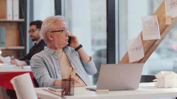 Elderly Male Architect Talking on Mobile Phone at Workplace