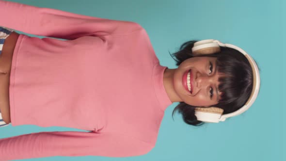 Young Mixed Race Woman Smiles Broadly Listens Music in Headphones Over Blue Wall