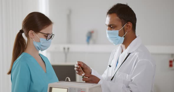 Side View of Indian Doctor in Safety Mask Showing Young Nurse How to Use Electrodes for Ecg