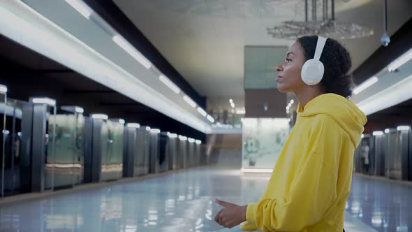 Young Girl Wearing Headphones and Looking at Phone While Waiting for a Train