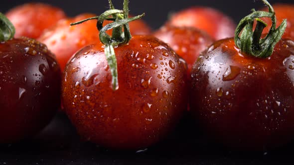 Cherry tomatoes on a black background in water drops.