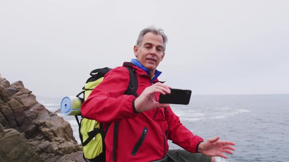 Senior hiker man with backpack standing on the rocks and taking a selfie on smartphone while hiking 