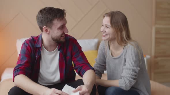 Husband and Wife are Sitting on Bed and Laughing at Each Other Front View