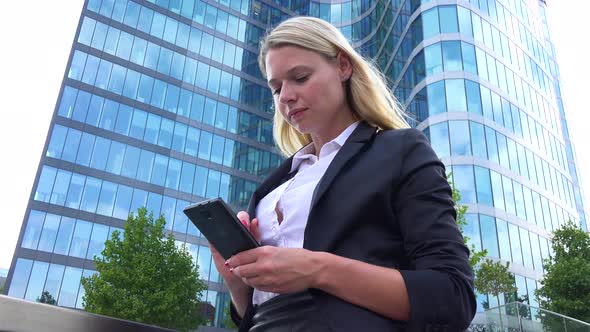 A Young Beautiful Businesswoman Works on a Smartphone - Closeup From Below - an Office Building