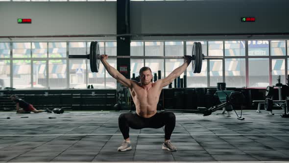 Young male athlete lifts a barbell above his head, weight training