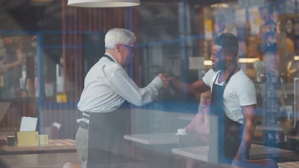 View Through Window of Two Diverse Owners of Coffee Shop in Aprons Shaking Hands