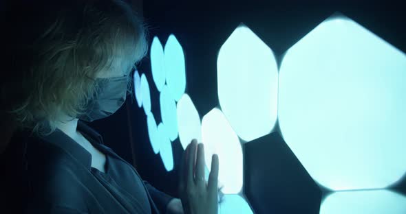 Portrait of a Curlyhaired Young Woman in a Black Protective Mask Touching a Light Touch Panel That