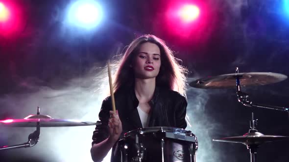 Girl Plays the Drums and Smiles. Black Smoke Background. Red Blue Light From Behind. Slow Motion