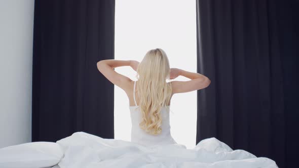 Young woman in the bed. Beautiful blond girl wakes up. Morning in the bedroom.