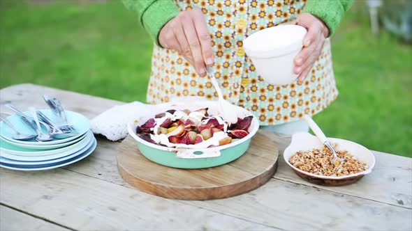 Woman putting creme and chopped nuts on fruit dessert