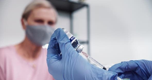 Closeup on Doctor Hand in Blue Glove Using Syringe and Vaccine Flask to Give Treatment Injection