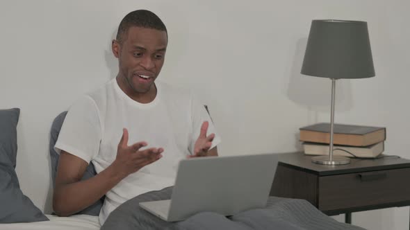 African Man Doing Video Call on Laptop in Bed