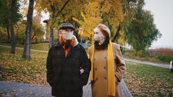 Elderly Pair Grandparents in Protective Masks are Talking During a Walk in Autumn Park Coronavirus