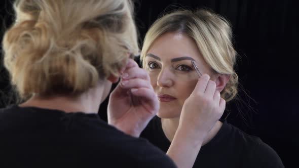 Woman Looks in the Mirror and Adjusts Her Eyebrows Tweezers. Close Up