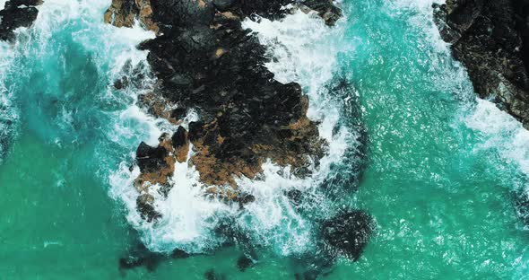 Static aerial shot looking directly below at waves crashing over rock.