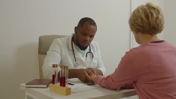 African Male General Practitioner Checking Heart Pulse Rate of Middle Aged Woman Patient at Office