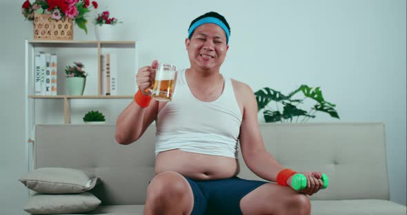 Overweight man in sportswear holding beer mug and dumbbell