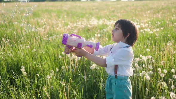 Portrait of a Five Year Old Boy in a Hat Stands on a Field of Dandelions and Shoots Soap Bubbles