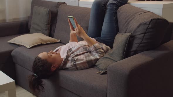 Woman Online Messaging Using Mobile App Via Internet on Couch Indoors