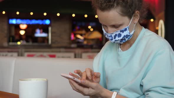 Young Woman Wearing Face Mask Using Her Smartphone in Coffee Placea at Her Coffee Break