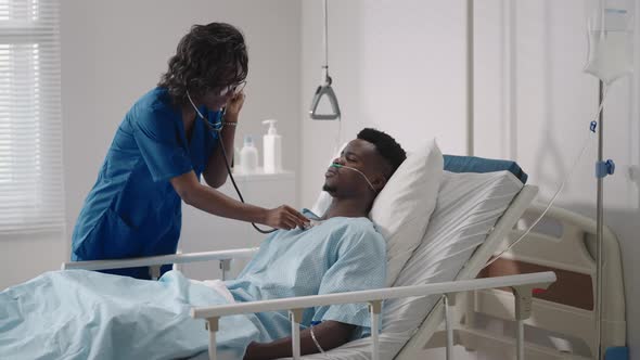 A Girl Doctor Examines and Talks to a Patient Lying on a Hospital Bed