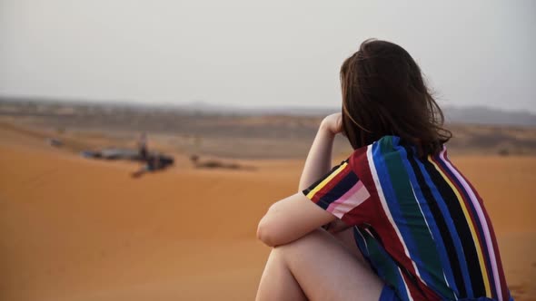 Young woman sitting in the sand of the Sahara desert contemplation concept. Morocco North Africa.