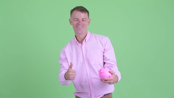 Happy Businessman Holding Piggy Bank and Giving Thumbs Up