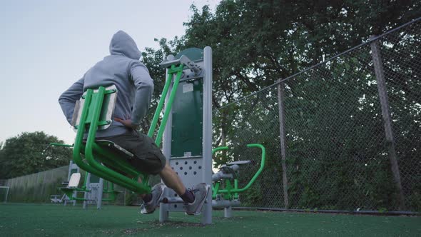Man using a leg press machine. Evening workout in an outdoor gym. Health and fitness