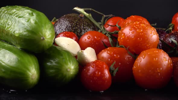 Cherry tomatoes, cucumbers, garlic, avocado and red onion on a black background in water drops