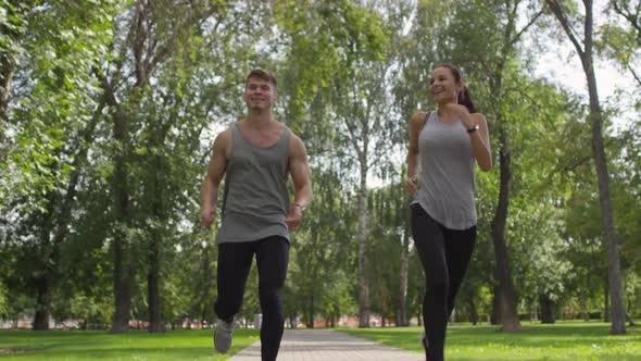 Young Cheerful Man and Woman Jogging in Park on Summer Day