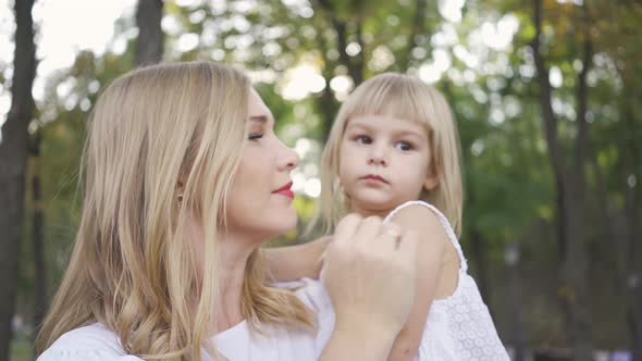 Portrait of Young Blond Woman in White Dress Caressing Her Cute Daughter